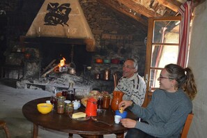Un intérieur rustique avec une cheminée en pierre, des poutres en bois et une table mise pour le repas.
