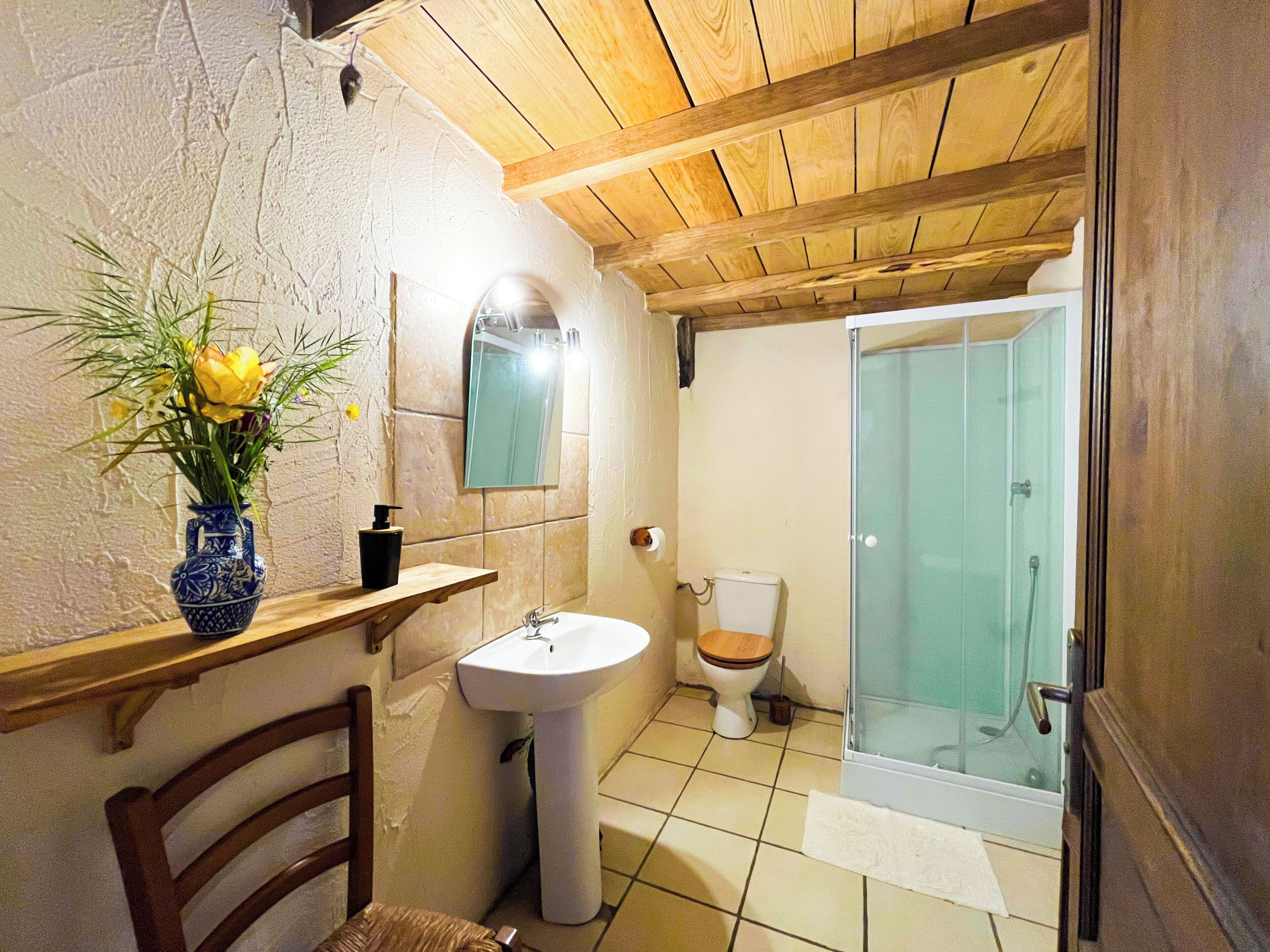 A bathroom with a wooden ceiling, a sink, a toilet, and a glass shower enclosure.
