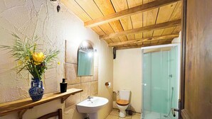 Un baño con techo de madera, lavamanos, inodoro y cabina de ducha de vidrio.