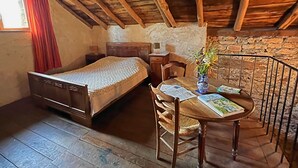 A rustic room with a wooden ceiling, a bed, a table with a vase, and a chair. - La ferme des Cévennes (Florac)