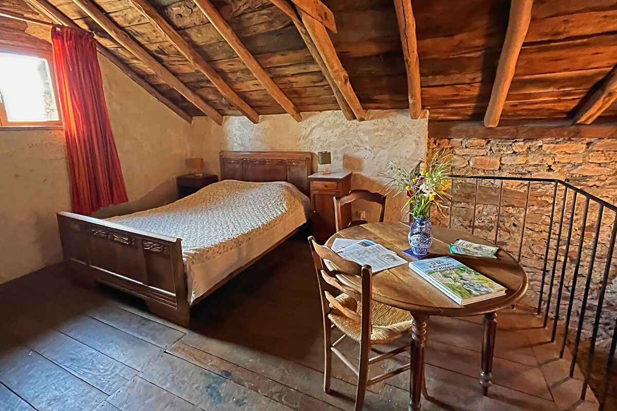 Une pièce rustique avec un plafond en bois, un lit, une table ornée d’un vase et une chaise.