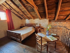 Una habitación rústica con techo de madera, una cama, una mesa con un florero y una silla.
