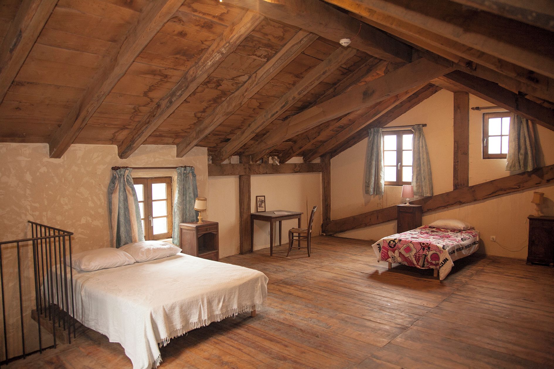 A rustic attic bedroom with a wooden ceiling, a bed, a desk, and a small table.