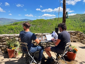 Dos personas sentadas en una mesa con vistas a colinas verdes y un cielo despejado.