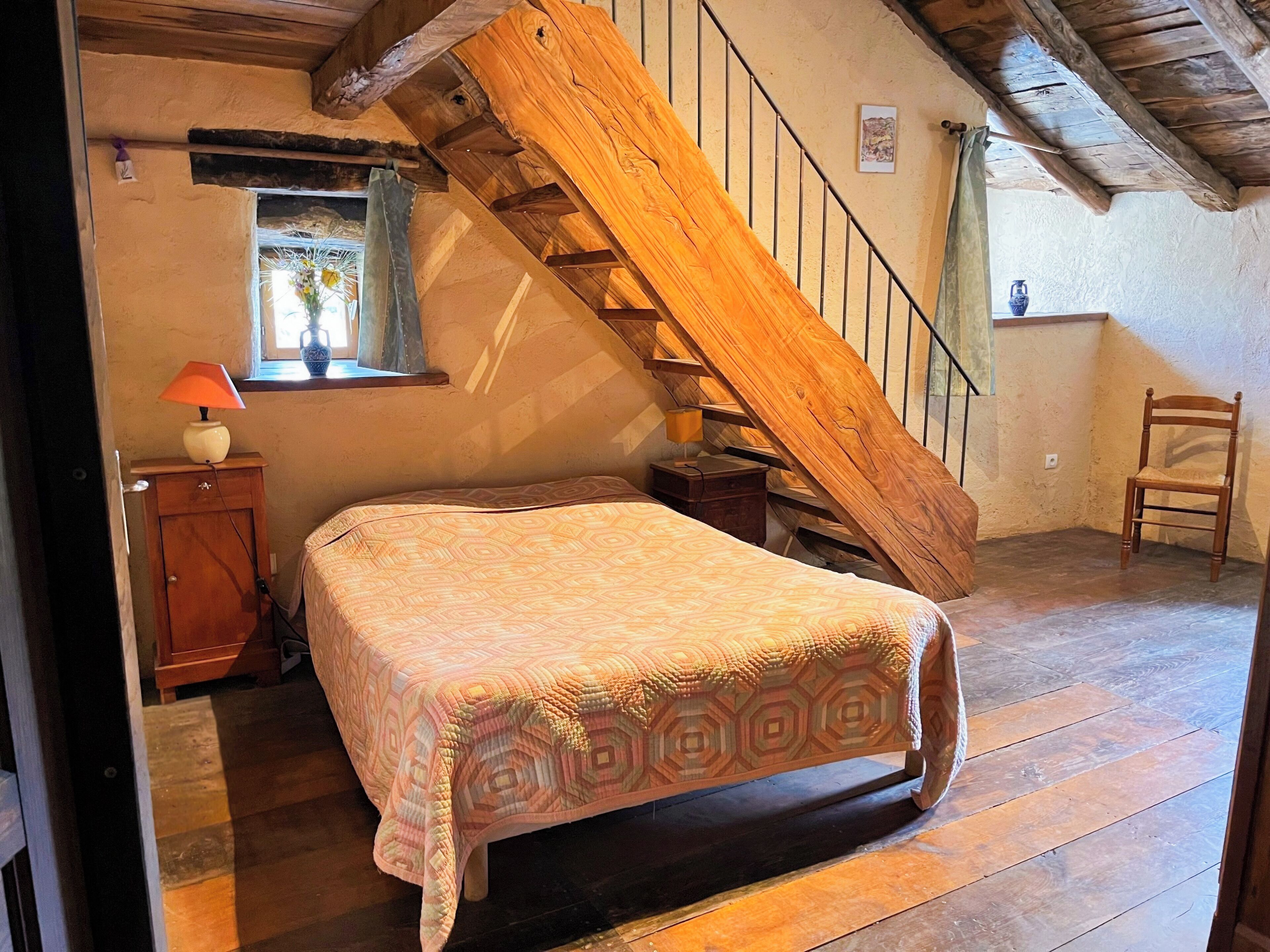 Un dormitorio con una escalera de madera, una cama con cubrecama estampado, una mesita de noche, una lámpara y una ventana con cortina.