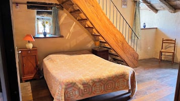 Un dormitorio con una escalera de madera, una cama con cubrecama estampado, una mesita de noche, una lámpara y una ventana con cortina.