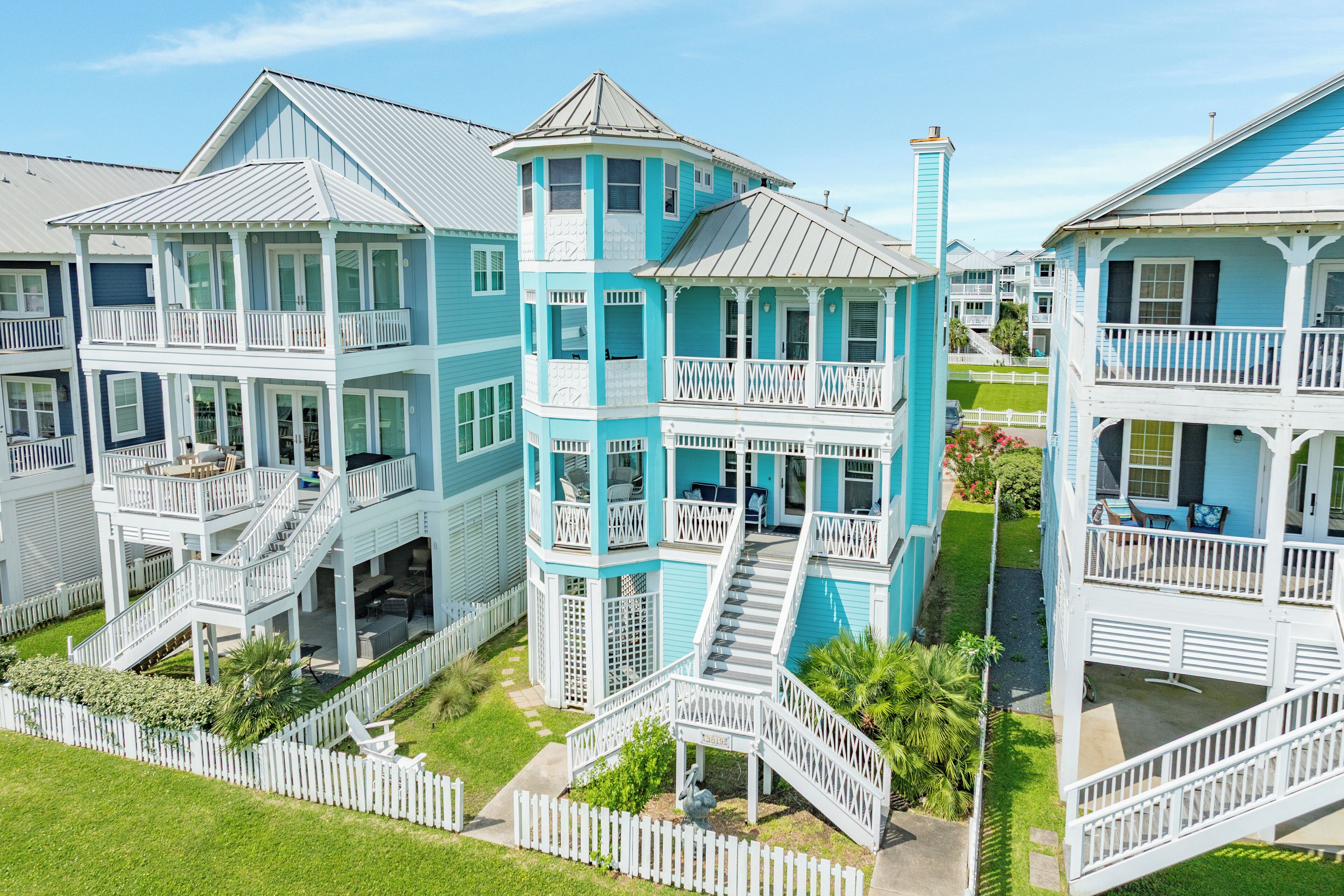 A multi-story beachfront property with balconies, a central tower, and a white picket fence.