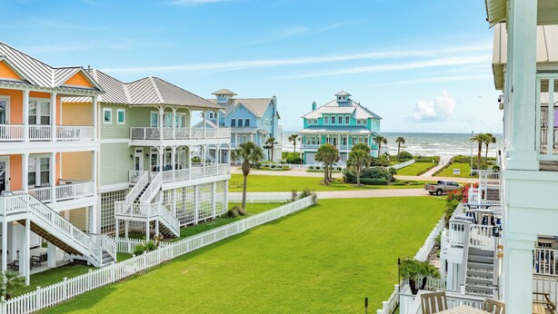 A beachfront hotel with multiple colorful buildings, a well-maintained lawn, and a view of the ocean. - Pet Friendly, Easy Walk to Beach, Game Room, Beach Toys, Gorgeous Community (Galveston)
