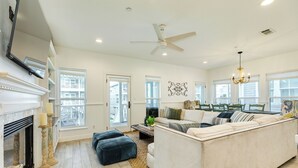 A spacious living room with a fireplace, a large sofa, and a dining area with a chandelier. - Pet Friendly, Easy Walk to Beach, Game Room, Beach Toys, Gorgeous Community (Galveston)
