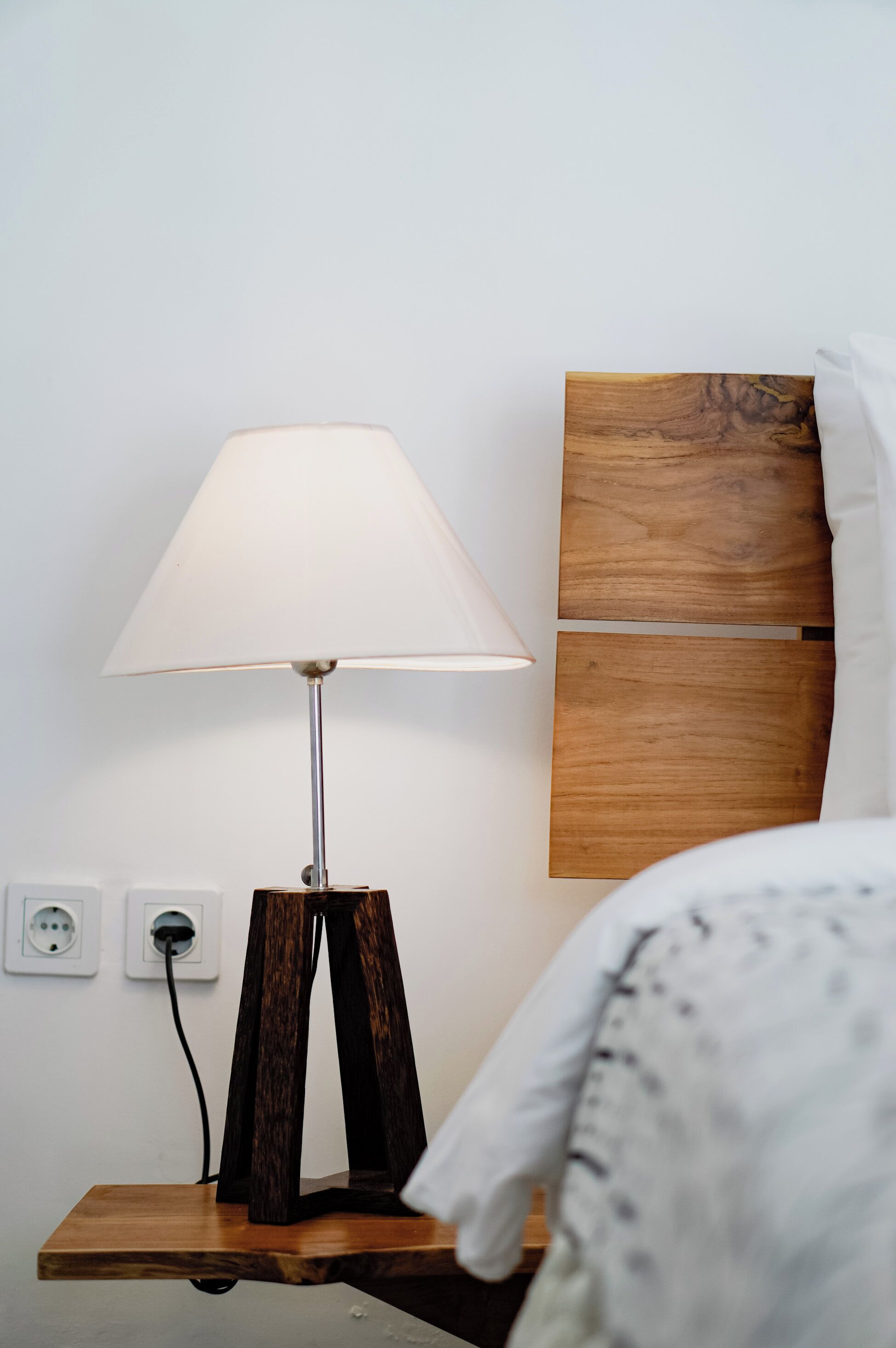 A bedside table with a lamp, a power outlet, and a wooden headboard.