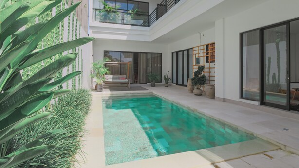 Une maison moderne à plusieurs niveaux, dotée d’une piscine, de grandes fenêtres et de plantes d’intérieur.