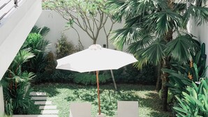 Une terrasse avec deux chaises longues blanches et un grand parasol, entourée d’une végétation luxuriante et d’une petite piscine.