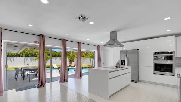 Egy modern konyha fehér szekrényekkel, rozsdamentes acélból készült háztartási gépekkel és egy nagy konyhaszigettel.