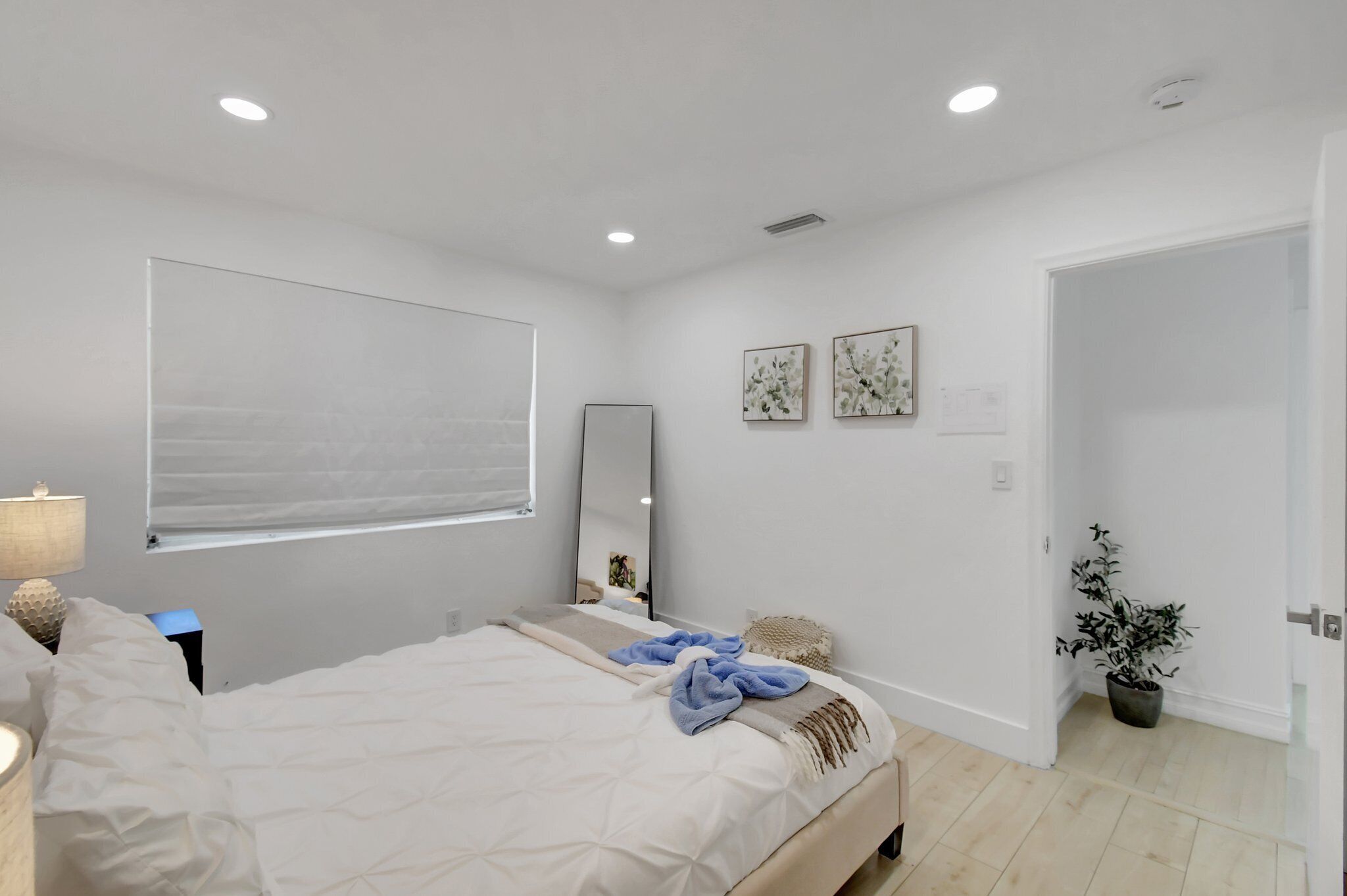 Une chambre moderne avec un grand lit, une lampe de chevet, un miroir et une plante en pot.