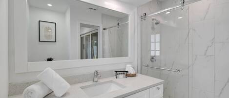 A modern bathroom with a large mirror, two sinks, a shower area, and a towel on the counter.