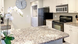 Une cuisine moderne avec des meubles blancs, un plan de travail en granit, des appareils électroménagers en acier inoxydable et une grande horloge murale.