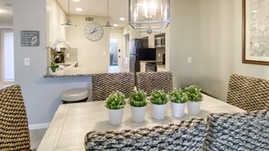 Une cuisine moderne dotée d’appareils électroménagers en acier inoxydable, un coin repas avec une table en bois et des coussins à motifs, ainsi qu’un luminaire suspendu.