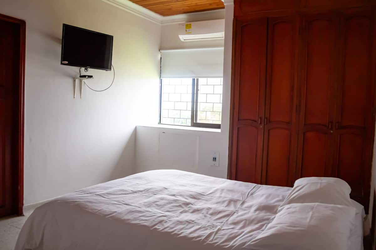 A bedroom with a bed, a television mounted on the wall, a window, and wooden wardrobes.
