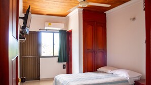 Ein Schlafzimmer mit zwei Betten, einem Deckenventilator, einer Klimaanlage und einem Fenster mit Vorhängen.