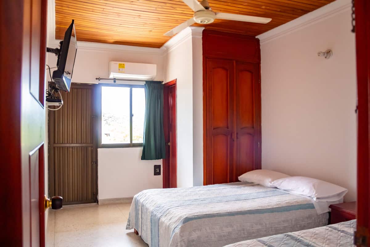 A bedroom with two beds, a ceiling fan, an air conditioning unit, and a window with curtains.