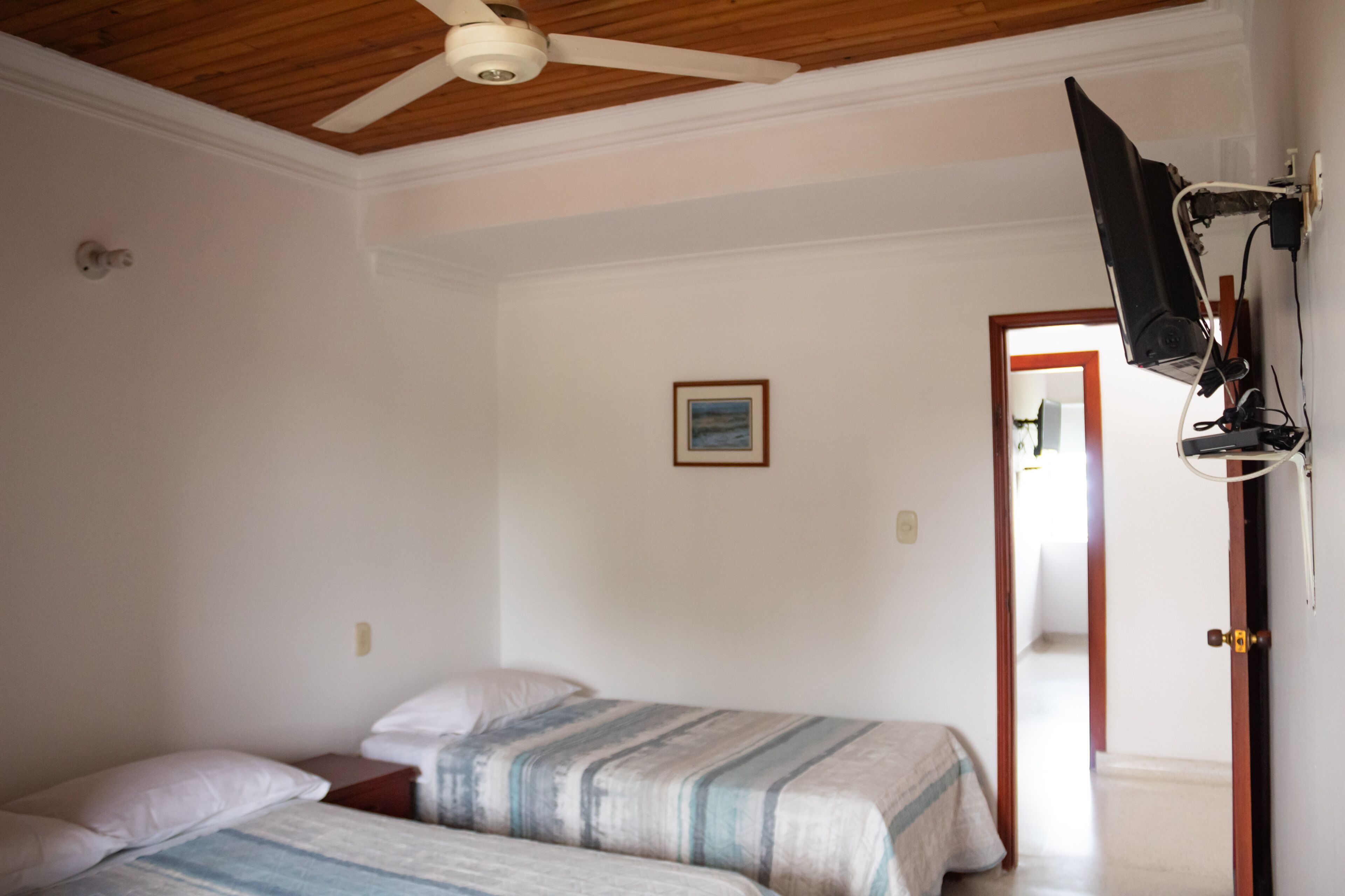 A bedroom with two beds, a ceiling fan, a television mounted on the wall, and a door leading to another room.