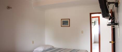 Un dormitorio con dos camas, un ventilador de techo, un televisor montado en la pared y una puerta que da a otra habitación.