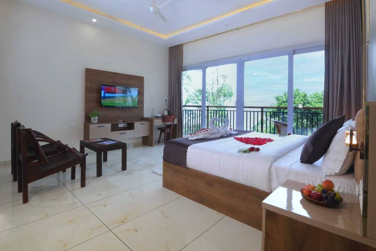 Ein Hotelzimmer mit einem großen Bett, einem Schreibtisch, einem Fernseher und einem Balkon mit Blick.