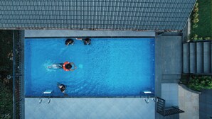 An aerial view of a rectangular swimming pool with four people in the water, surrounded by a metal fence and a tiled deck. - EVAARA RESORT (Devikolam)