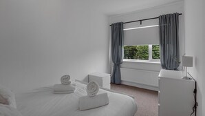 Une chambre d’hôtel au style minimaliste, avec un grand lit, une table de chevet, une lampe et une fenêtre avec des rideaux.