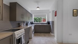 Une cuisine moderne avec des meubles gris, un four encastré, un lave-linge et une fenêtre donnant sur un espace verdoyant.
