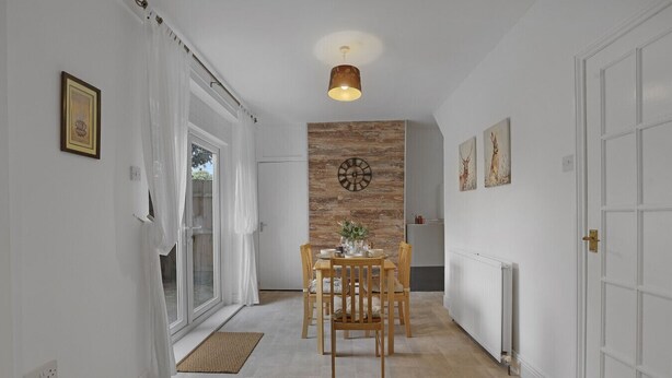 Un couloir avec un coin repas comprenant une table et des chaises en bois, une horloge au mur et un radiateur sur le côté droit.