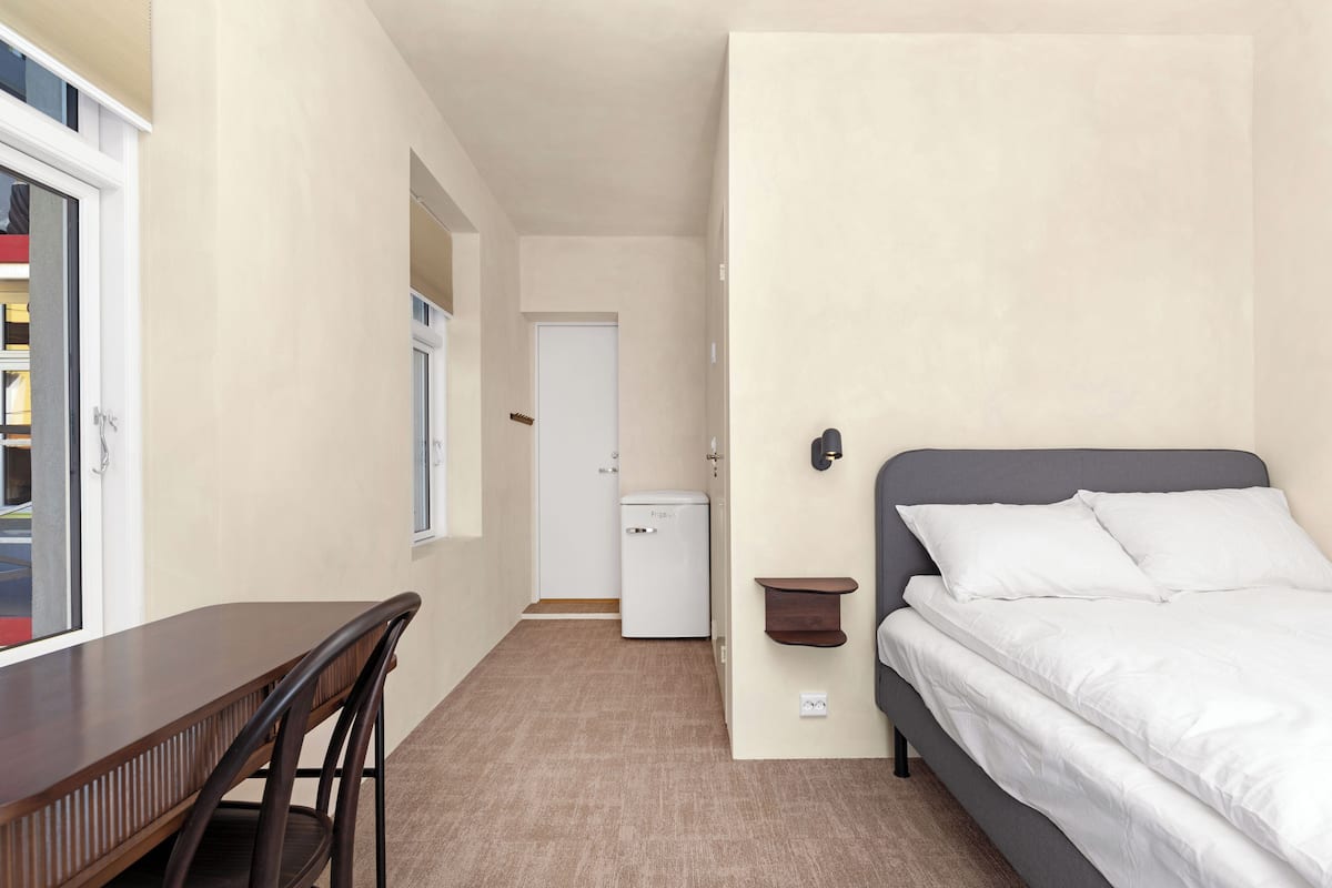 Une chambre à coucher avec un lit, un bureau et une chaise. Une porte donne accès à une autre pièce.