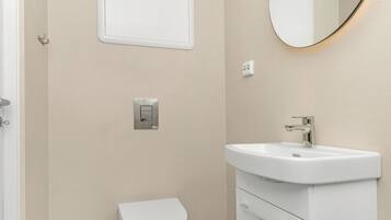 A bathroom with a toilet, a white sink, a mirror, and a light switch on the wall.