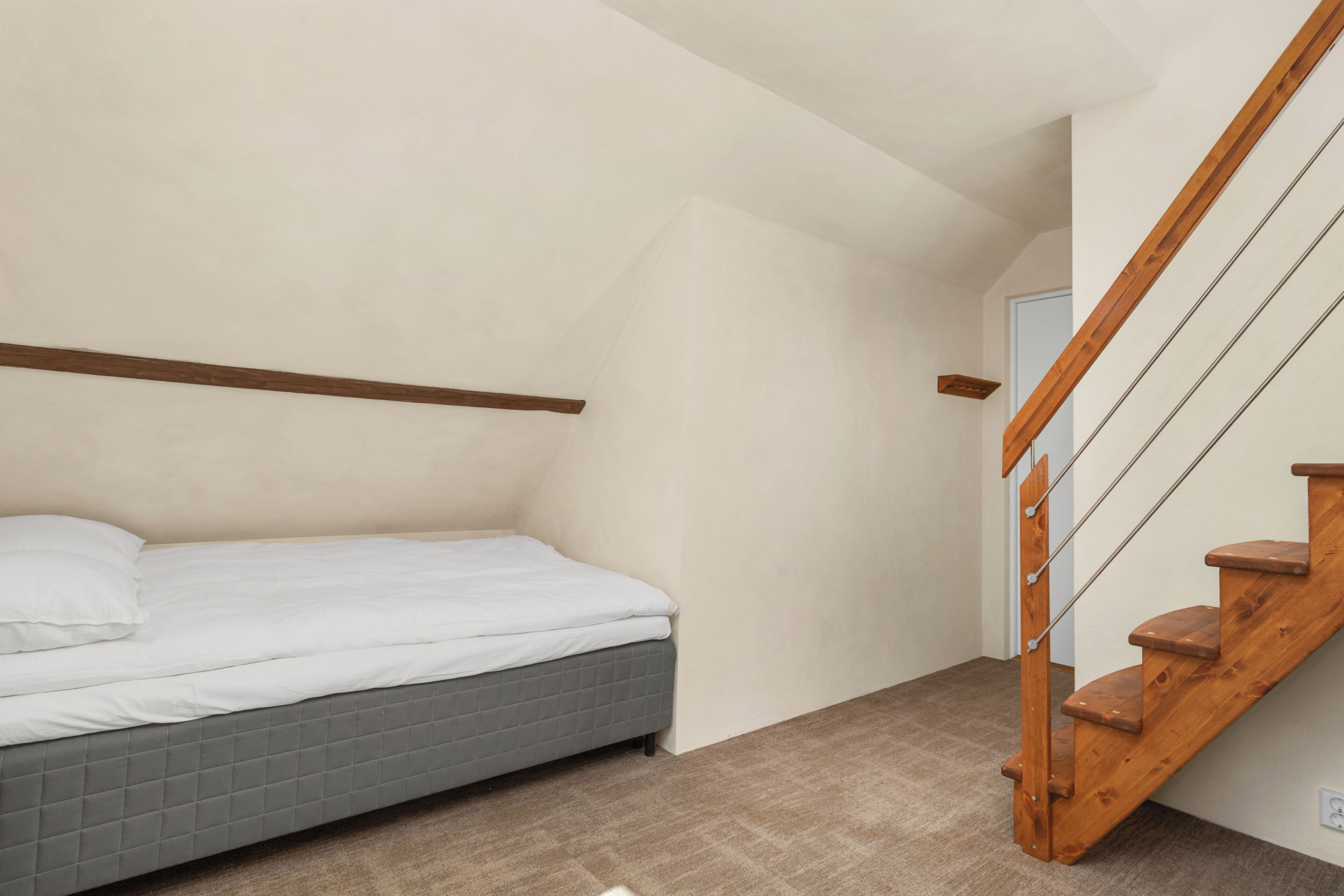 Un dormitorio con una cama, una escalera de madera y una puerta al fondo.