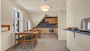A modern kitchen with wooden cabinets, a built-in oven, and a dining area with wooden tables and chairs. - Central Guest House - Private Bathroom (Stavanger)