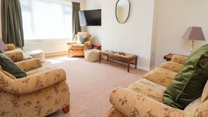 A living room with floral-patterned sofas, a television, a mirror, and a lamp. - Bryn Bach (Colwyn Bay)