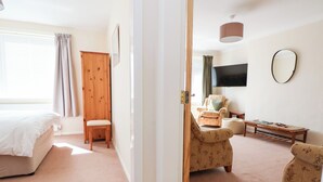 A bedroom with a bed, a wooden wardrobe, a chair, a sofa, a TV, and a mirror. - Bryn Bach (Colwyn Bay)