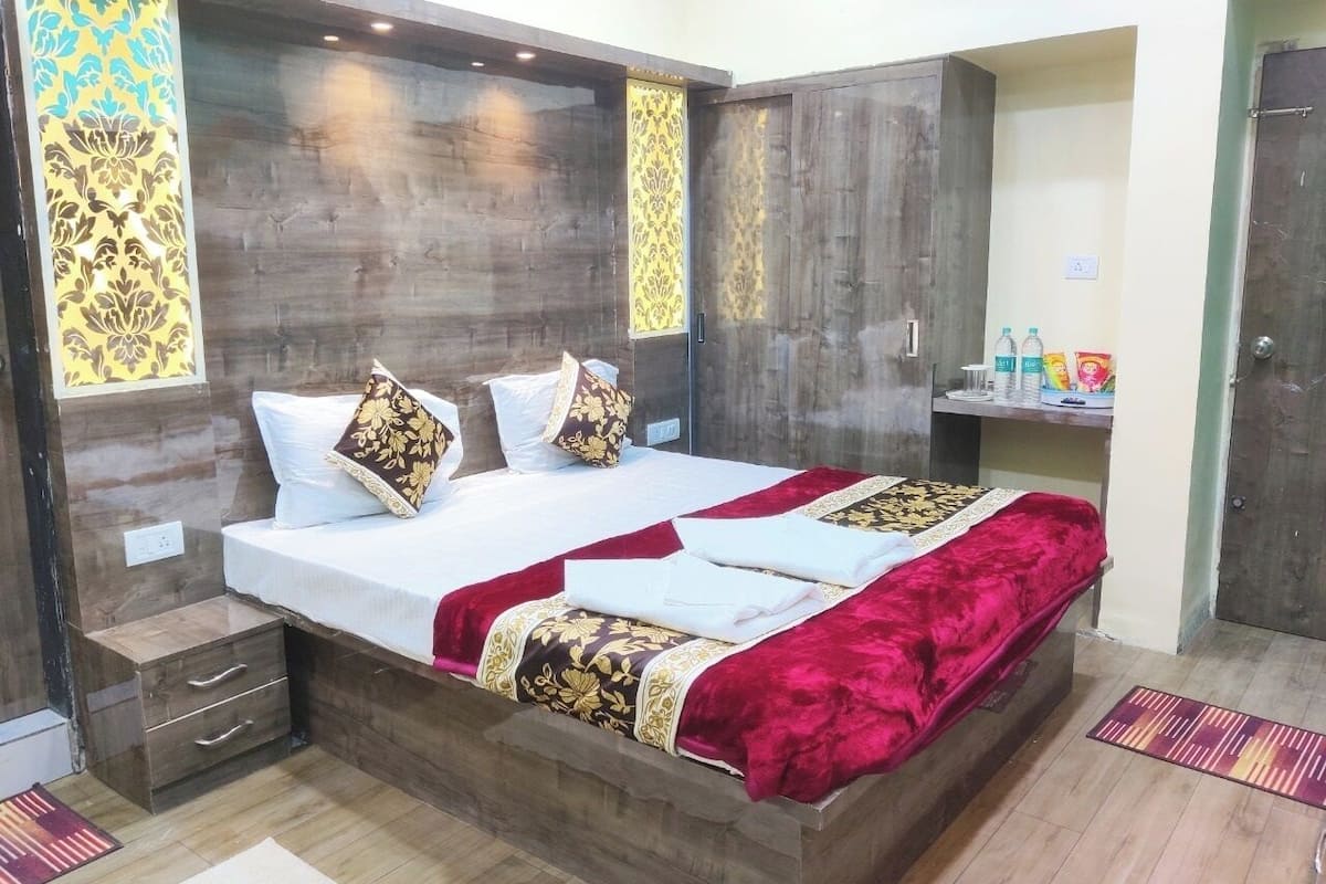 Cama doble con edredón rojo y dorado, cabecero de madera y dos mesitas de noche con cajones.
