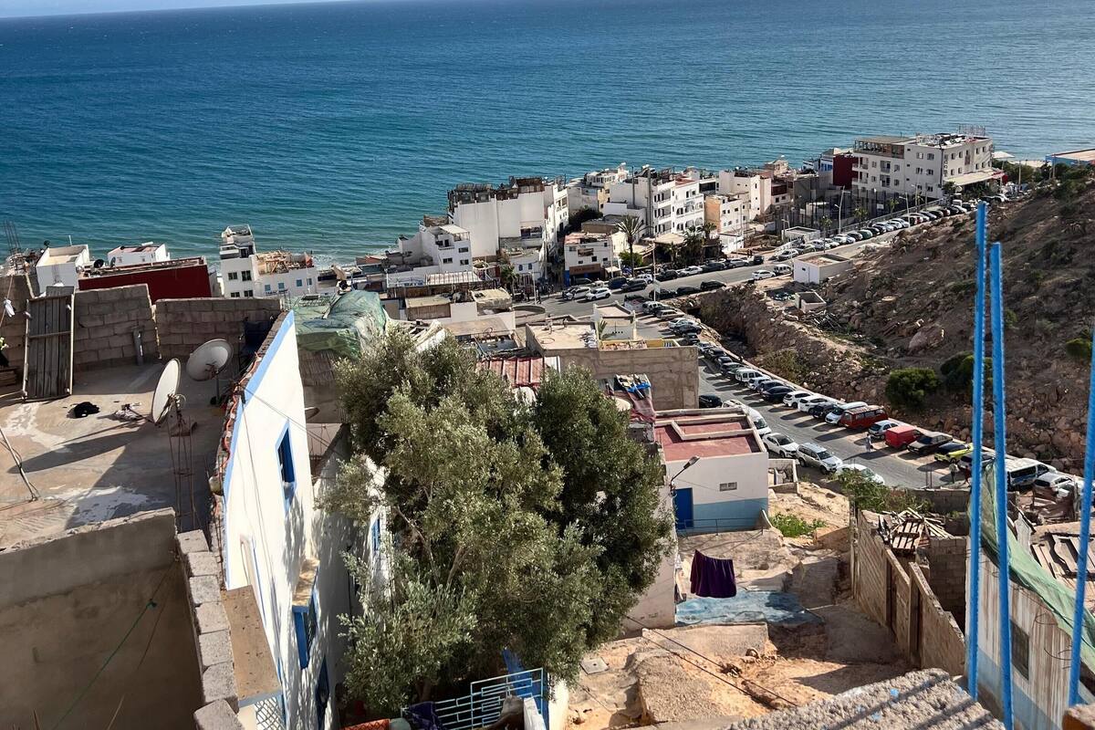 A coastal town with buildings along the sea, a parking area, and a view of the ocean.