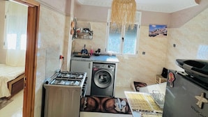 A compact kitchen with a gas stove, a washing machine, and a refrigerator.