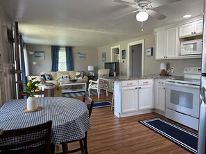 A modern kitchen with white cabinets, a built-in oven, and a microwave. There's a dining area with a checkered tablecloth and chairs.