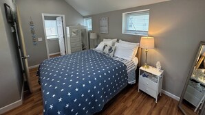 Een slaapkamer met een bed, nachtkastjes, een dressoir, een plafondventilator en een raam met jaloezieën.