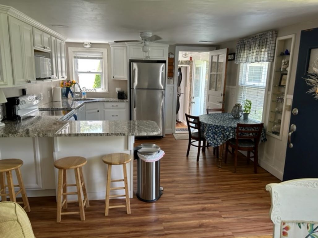 A kitchen with wooden stools, a refrigerator, and a trash can.
