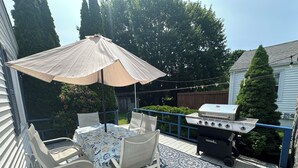 Een terras met een tafel, stoelen, een barbecue en een parasol.