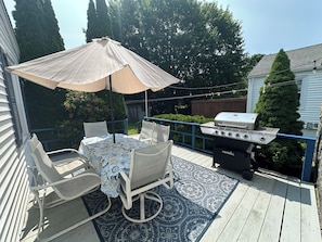 A patio with a table, chairs, a grill, and an umbrella.