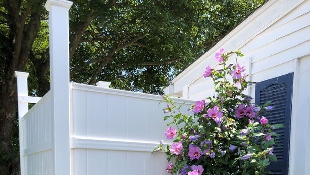 Een wit houten terras, grenzend aan een gebouw met een witte omheining.