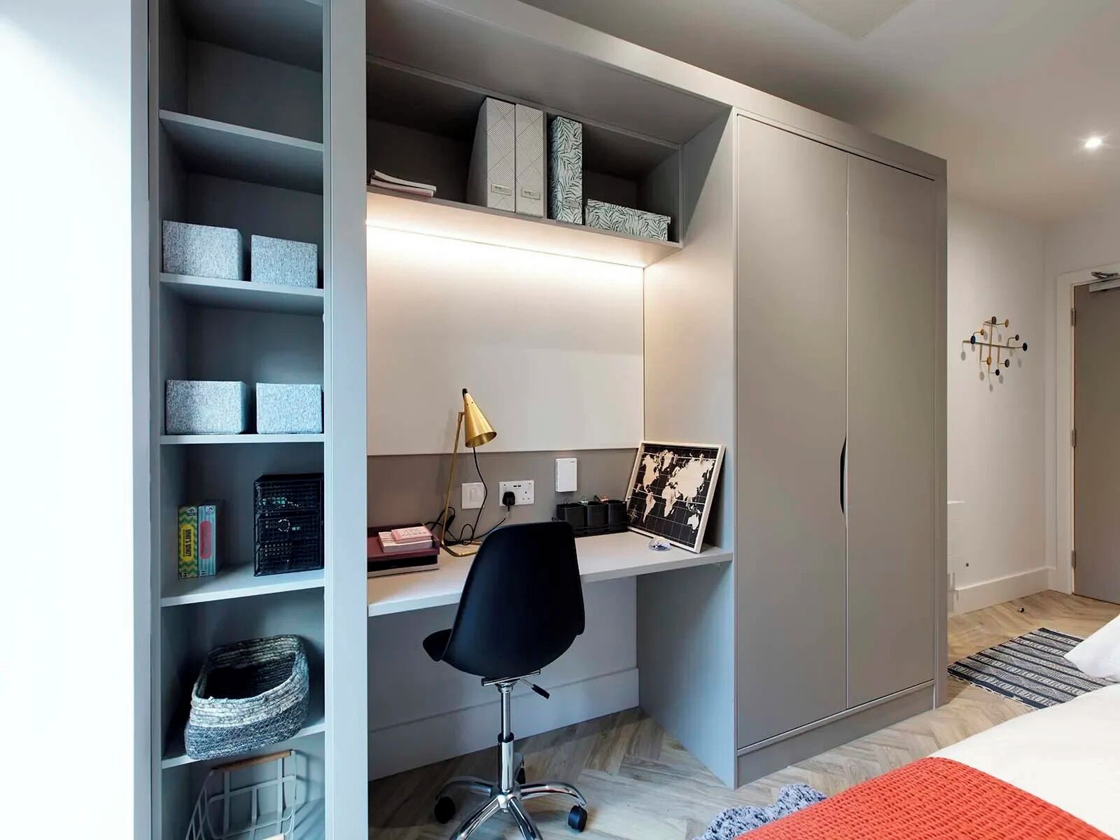 Un dormitorio moderno con un armario gris, un escritorio con lámpara y una cama con una colcha roja.