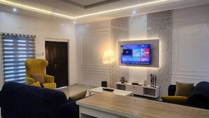 Un salon moderne avec un téléviseur à écran plat fixé au mur, un fauteuil jaune, un canapé foncé et une table basse en bois.