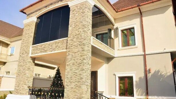 Une maison à deux étages avec une façade en pierre, une grande baie vitrée et un balcon.