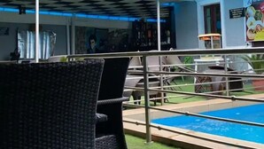 Un espace aménagé au bord de la piscine, avec un plafond à carreaux, une chaise en osier et une piscine dotée d’une rambarde en métal.
